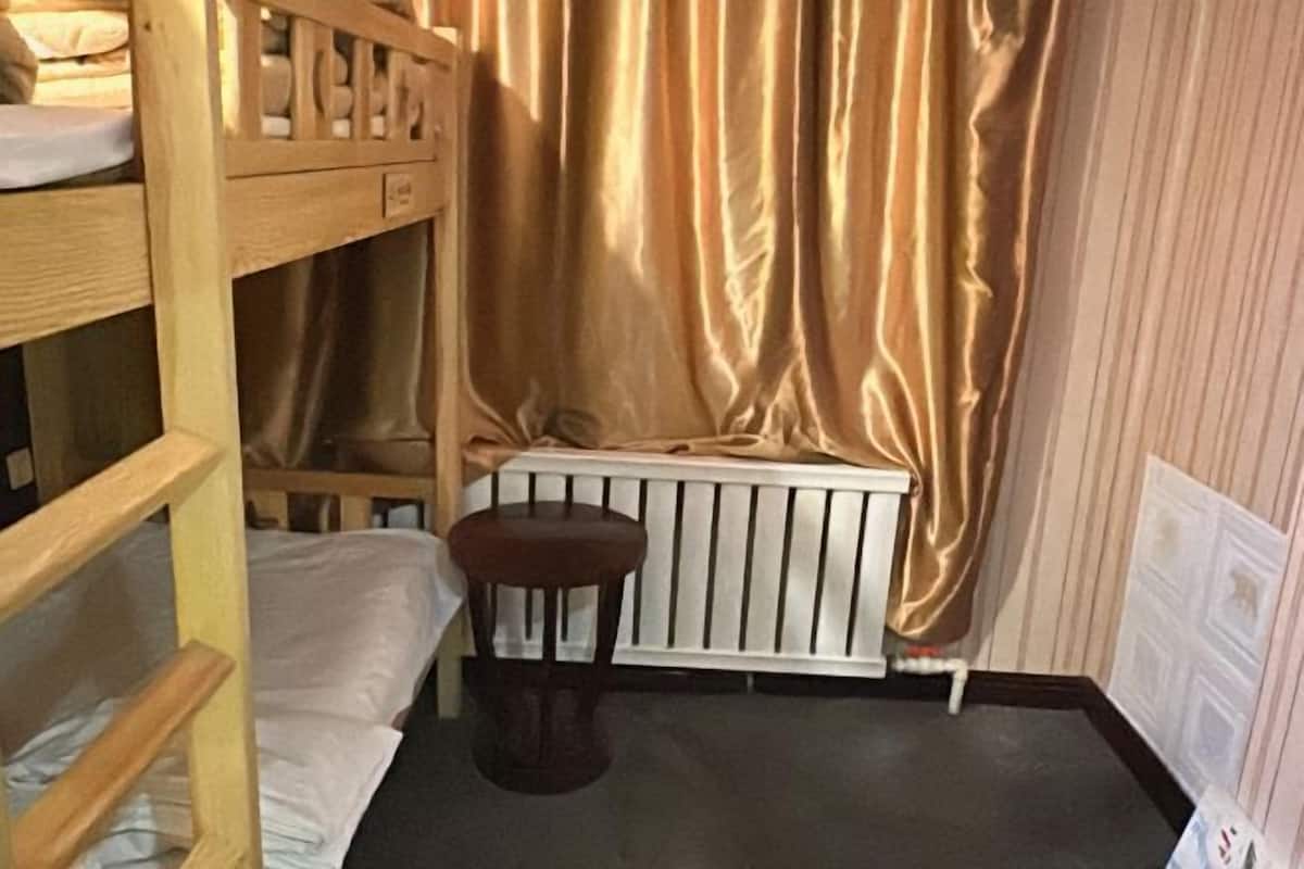 Quarto com beliche, um radiador, um banquinho e uma cortina.