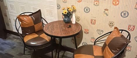A room with two metal chairs with brown cushions, a small round table with a vase of sunflowers, and a wall decorated with various sports team logos.