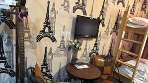 A room with a bed, a TV mounted on the wall, a round table with chairs, and a bookshelf. - Not Alone Minyao Youth Hostel (Shenyang)