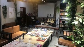 A room with a long table displaying various items, a piano, and a stage with musical instruments. - Not Alone Minyao Youth Hostel (Shenyang)
