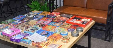 A table with various board games and books, a brown leather couch, and a plant in the background.