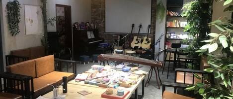 A room with a long table displaying various items, a piano, and a guitar in the background.