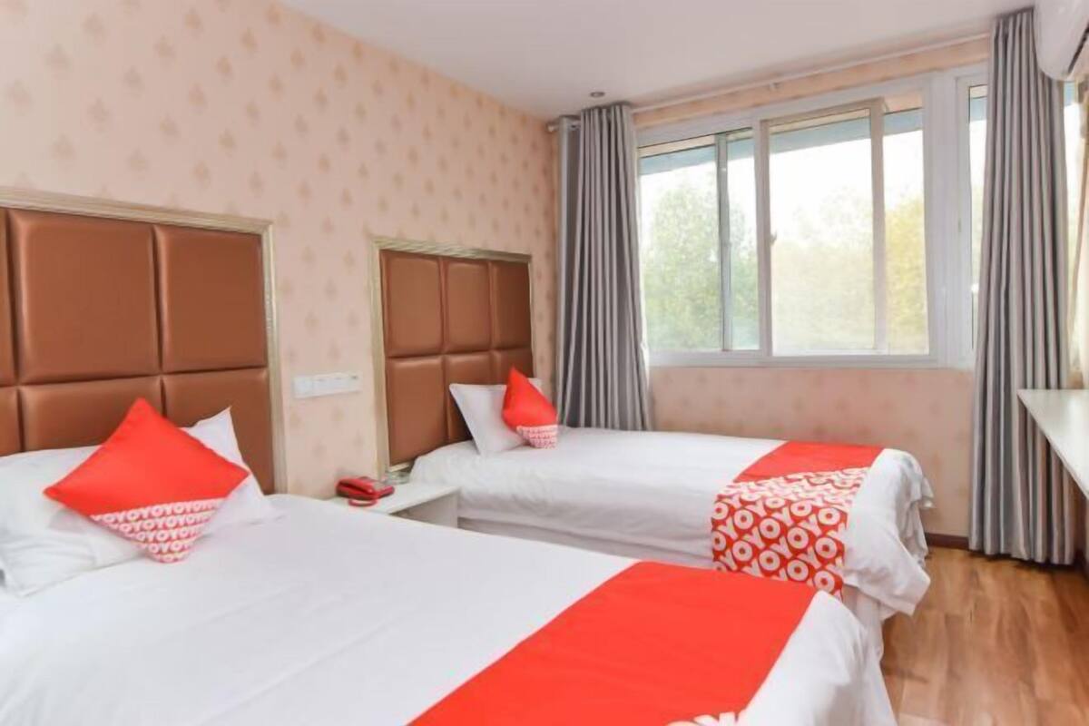 Una habitación de hotel con dos camas, una ventana con cortinas y suelo de madera.