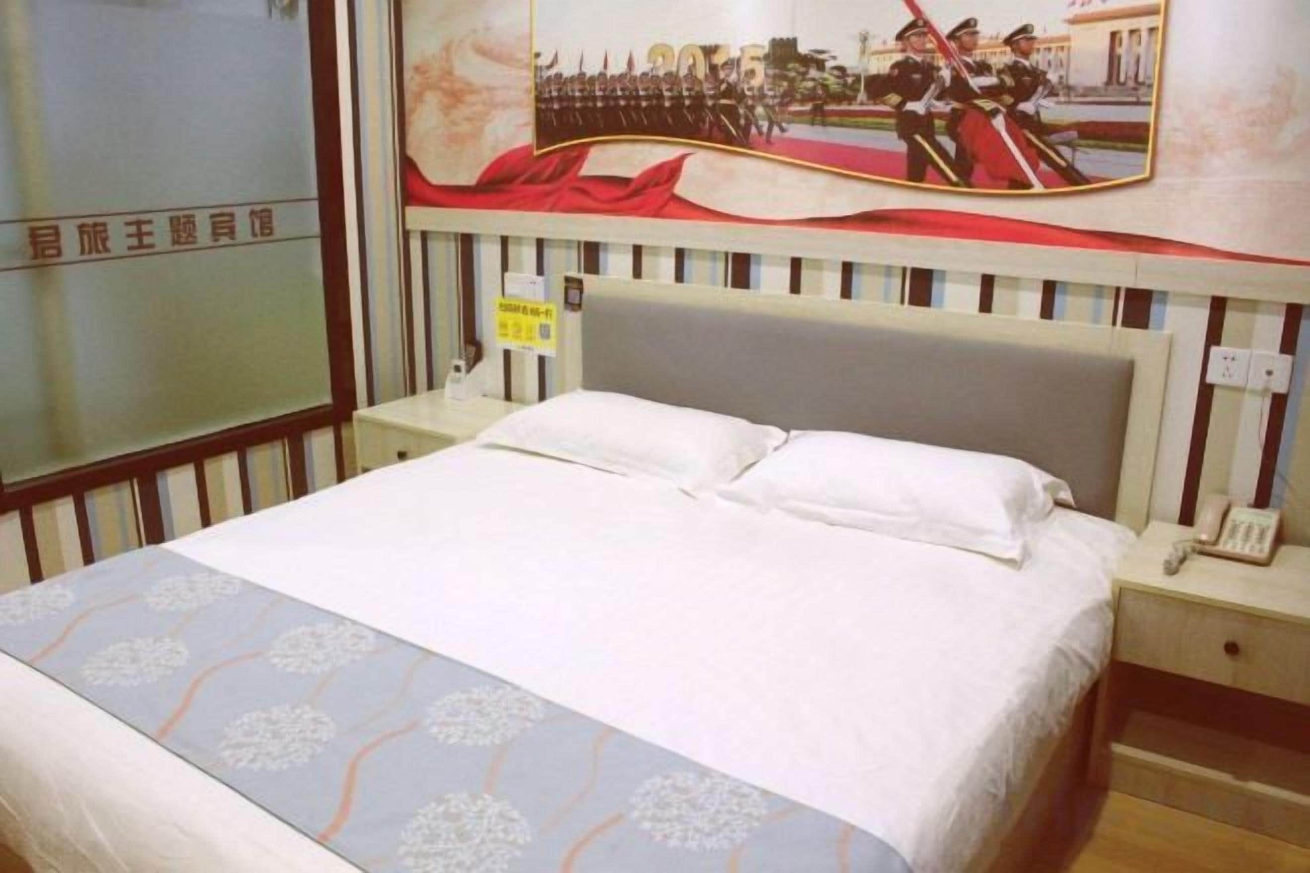 A hotel room with a bed, a nightstand with a phone, and a wall with a poster.
