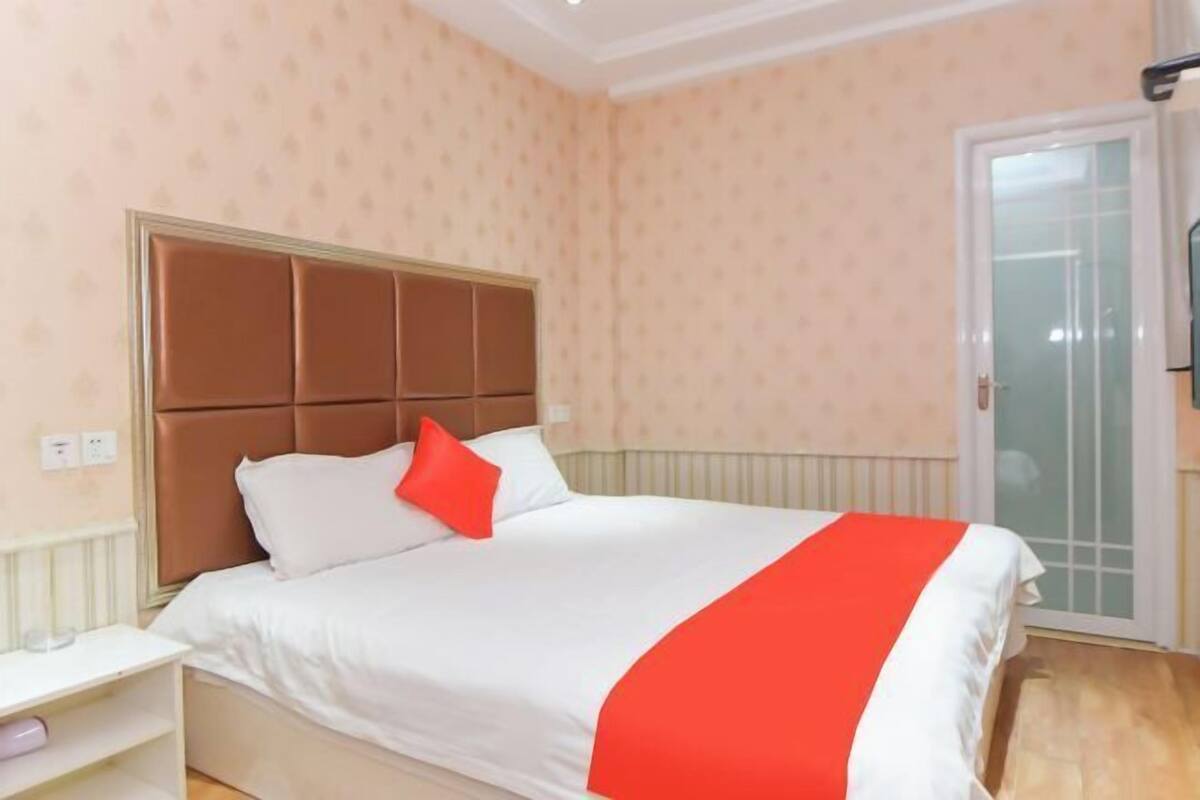 Una cama bien hecha con cabecera, una mesita de noche y una manta roja.