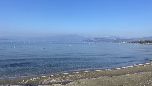 Une vue sur la côte, avec un ciel dégagé, une mer calme et des montagnes à l’horizon.