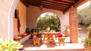 Une terrasse extérieure avec des tables et des bancs en bois, une colonne en briques et des plantes en pot.
