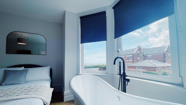 Un dormitorio moderno con un ventanal grande, una bañera y una cama con cabecero.