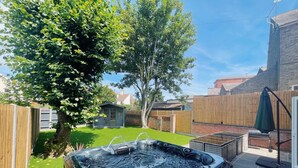 Un jacuzzi en un patio trasero con una cerca de madera, un árbol y un cobertizo pequeño.