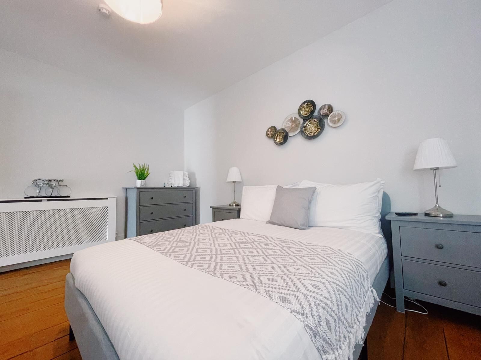 A bedroom with a large bed, a dresser, a bedside table, a lamp, and decorative wall art.