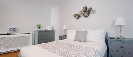 A bedroom with a large bed, a dresser, a bedside table, a lamp, and decorative wall art.