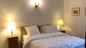 A bedroom with a bed, two bedside tables with lamps, a patterned rug, and a framed picture on the wall. - Les Anémones (Lamballe)