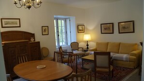 A cozy living room with a wooden dining table, chairs, a sofa, and a lamp. - Les Anémones (Lamballe)