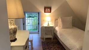 A bedroom with a bed, a nightstand, a dresser, a lamp, a window with a view of greenery, and a framed picture on the wall. - Les Anémones (Lamballe)