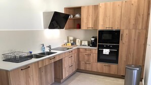 A modern kitchen with wooden cabinets, a stainless steel sink, a coffee maker, and a trash bin. - Les Anémones (Lamballe)