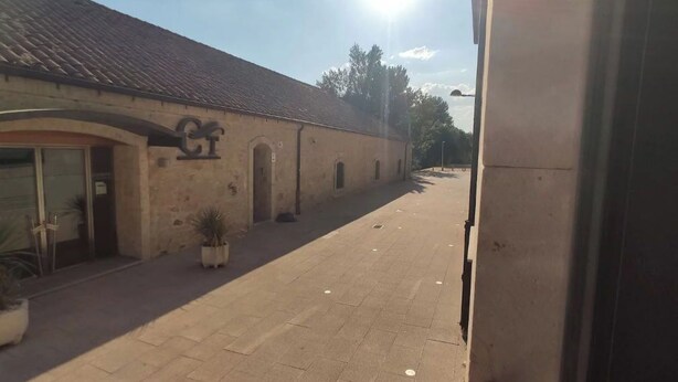 Un edificio con tejado de tejas y una entrada arqueada grande. Hay macetas con plantas a lo largo de la acera.