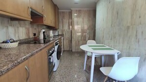 Cocina compacta con armarios de madera, encimera de granito, una mesa blanca con rayas verdes y una silla blanca.