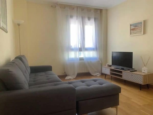 A living room with a grey sofa, a flat-screen TV on a wooden stand, a floor lamp, and a painting on the wall.