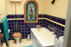 A bathroom with a toilet, bathtub, and a decorative stained glass window above the sink.