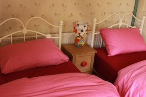 A bedroom with two beds, each with pink bedding and pillows. There is a wooden nightstand with a colorful globe and a red knob between the beds.