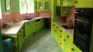 A kitchen with green cabinets, a black stove, and a window with pink polka dots on the wall. - Colourful Forest of Dean Pikehouse (Lydney)