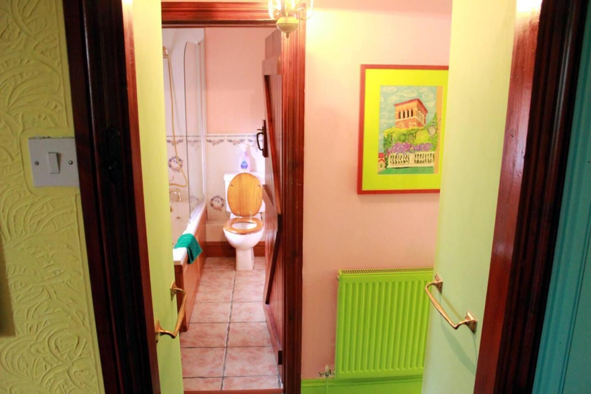 A narrow hallway leading to a bathroom with a toilet, a radiator, and a framed picture on the wall.