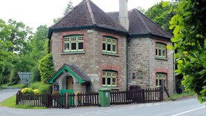 A stone house with a pitched roof, a chimney, and a small porch with a green door. - Colourful Forest of Dean Pikehouse (Lydney)