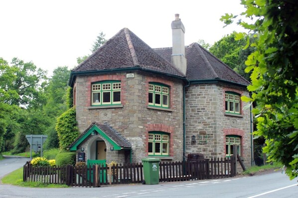 A stone house with a pitched roof, a chimney, and a small porch with a green door.