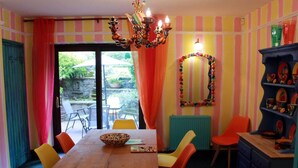 A dining area with a wooden table, orange chairs, and a colorful chandelier. - Colourful Forest of Dean Pikehouse (Lydney)