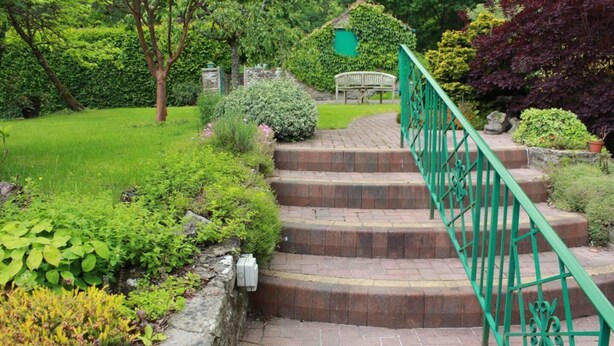 A set of brick stairs with a green metal railing leading up to a bench in a garden with various plants and a stone wall. - Colourful Forest of Dean Pikehouse (Lydney)