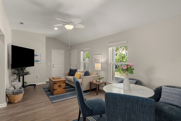 Ein modernes Wohnzimmer mit Flachbildfernseher, Deckenventilator, Esstisch und Sofa.