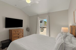 Ein Schlafzimmer mit einem Bett, einer Holzkommode, einem an der Wand montierten Fernseher und einem Fenster mit Vorhängen.