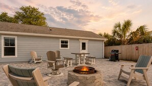 Un patio trasero con sillas Adirondack, un pozo de fuego y una zona de parrilla.
