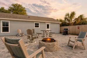 Eine Hinterhofterrasse mit Adirondack-Stühlen, einem Feuerkorb und Grillplatz.