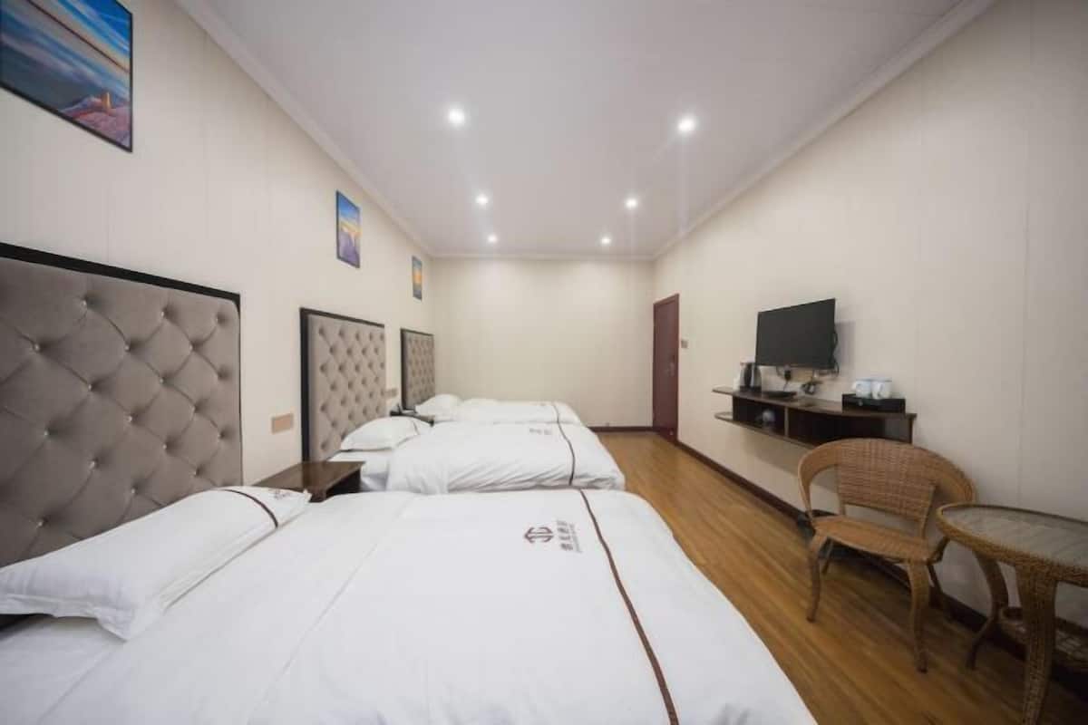 Une chambre d’hôtel avec trois lits, une télévision, une petite table et une chaise en osier.