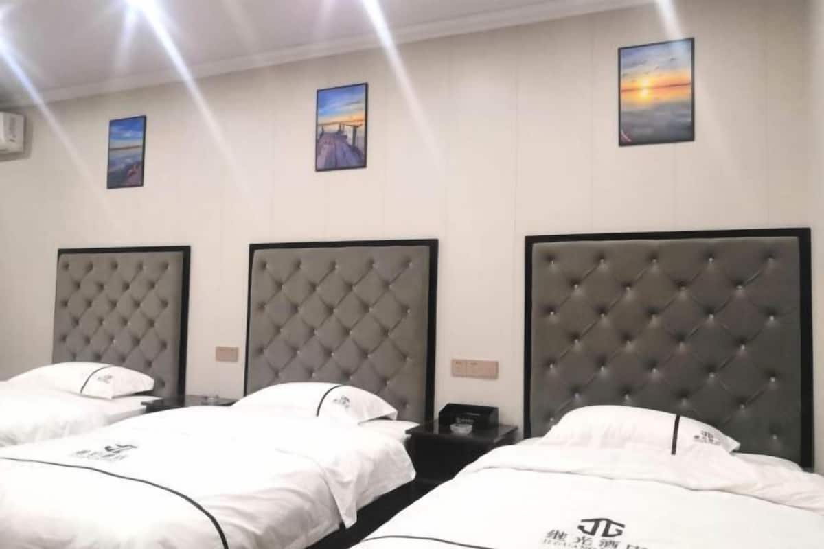 Une chambre d’hôtel avec trois lits, chacun doté d’une tête de lit capitonnée, de draps blancs et d’une petite table de chevet avec une lampe.