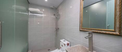 Un baño con cabina de ducha de vidrio, inodoro blanco, lavamanos de granito y espejo con marco dorado.
