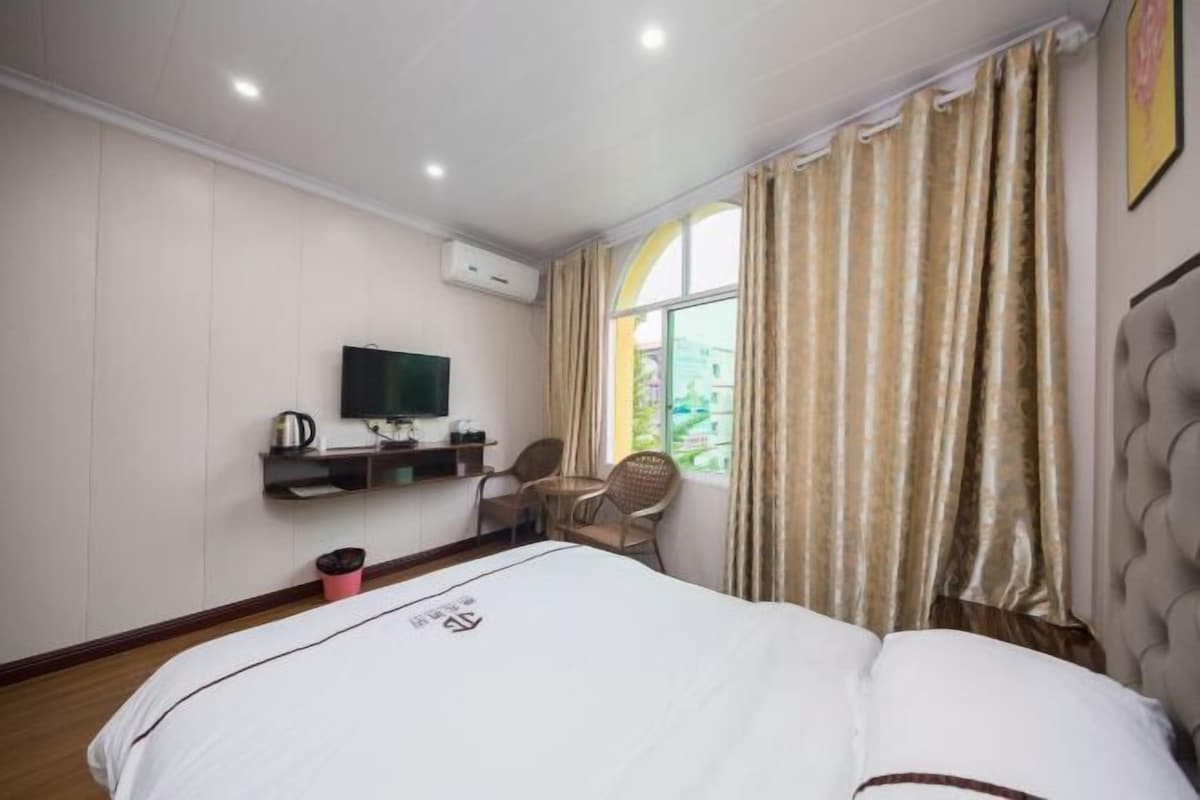 A hotel room with a bed, a TV, a chair, a small table, and a window with curtains.