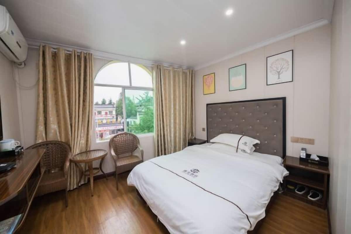 Une chambre d’hôtel avec un lit, un bureau, une chaise, une petite table et une fenêtre avec des rideaux.