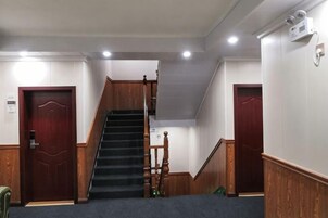 Um corredor de hotel com escadas de madeira, piso coberto por carpete e duas portas de madeira.