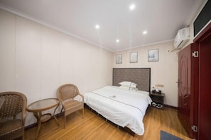 A bedroom with a bed, two wicker chairs, a small table, a nightstand, and a wardrobe. - Jiguang Hotel (Chongqing)