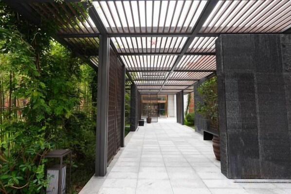 A covered walkway with a metal roof, surrounded by greenery and potted plants.