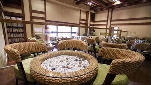 A room with woven chairs around a central table, a bookshelf, and a view through a window. - Zhaojin Shuyuan Hotel (Tongchuan)