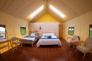 Una habitación tipo tienda con dos camas, un escritorio, sillas y una mesita.