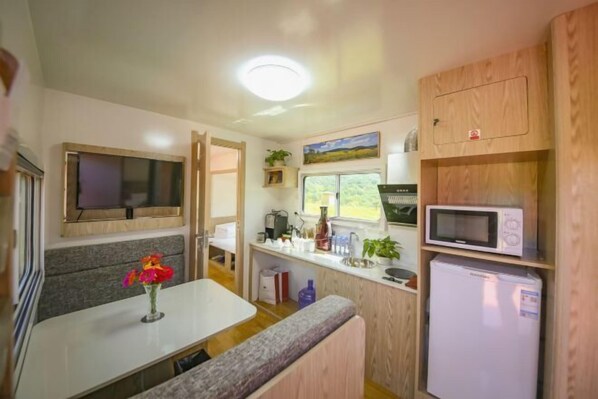 Una kitchenette compacta con microondas, refrigerador y un lavamanos pequeño.