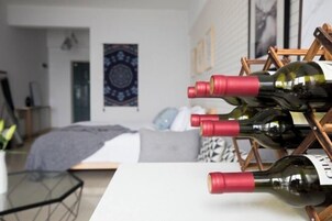 A room with a bed, a wooden wine rack holding several bottles, and a wall with a patterned tapestry.