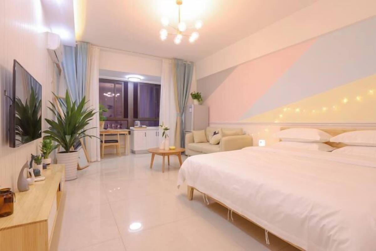 A modern hotel room with a large bed, a desk, a sofa, and a dining area.