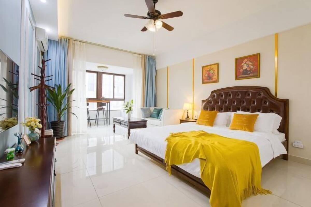 A hotel room with a bed, a desk, a chair, a ceiling fan, and a window.