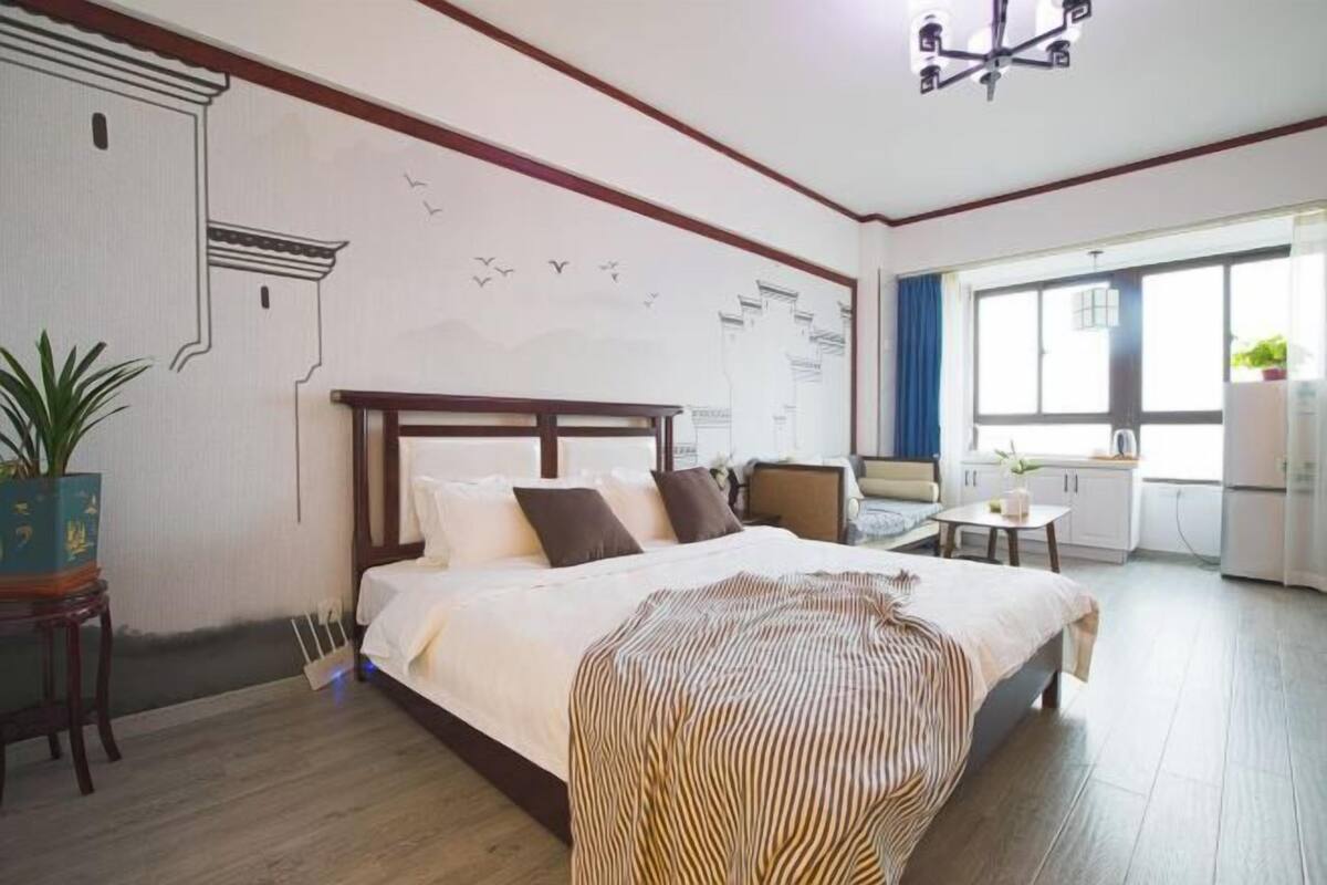 A hotel room with a large bed, a small table, a chair, and a window with curtains.