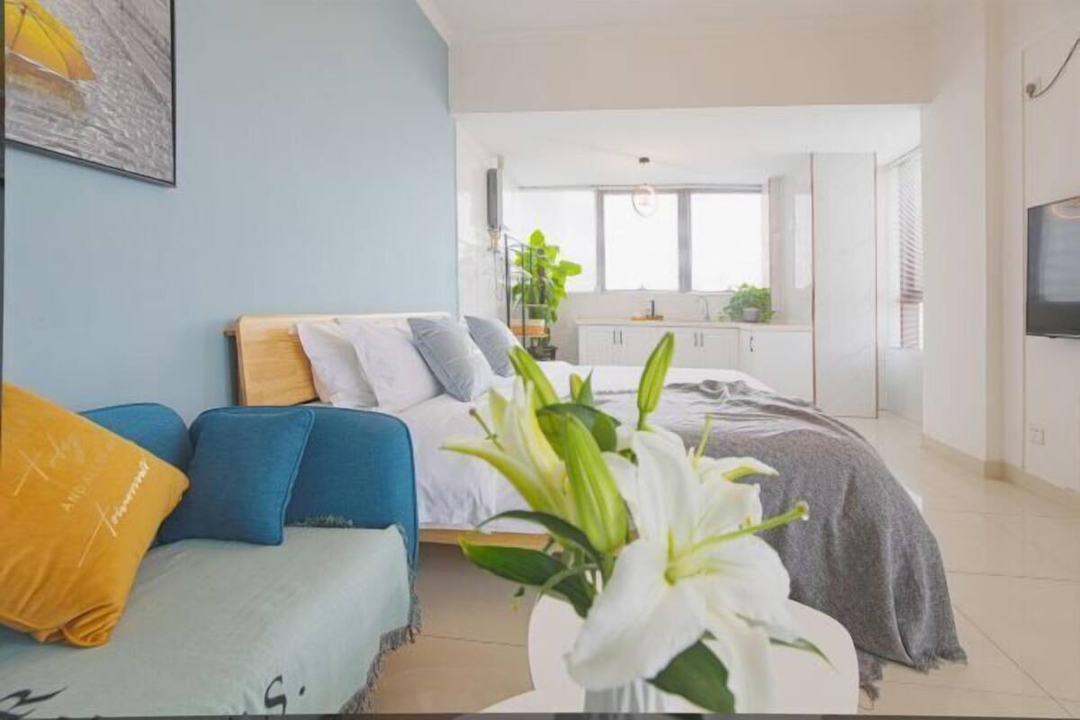 A modern bedroom with a bed, a sofa, and a dining area in the background.